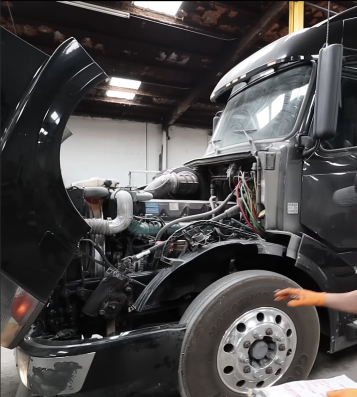 Semi truck with hood open showing diesel engine in a repair bay